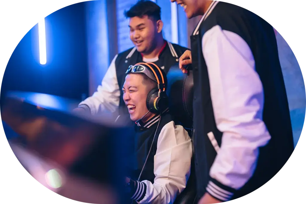 Drie vrienden in dezelfde jassen juichen en lachen terwijl ze gamen in een schemerige kamer met neonverlichting, wat zorgt voor een energieke en gezellige sfeer.